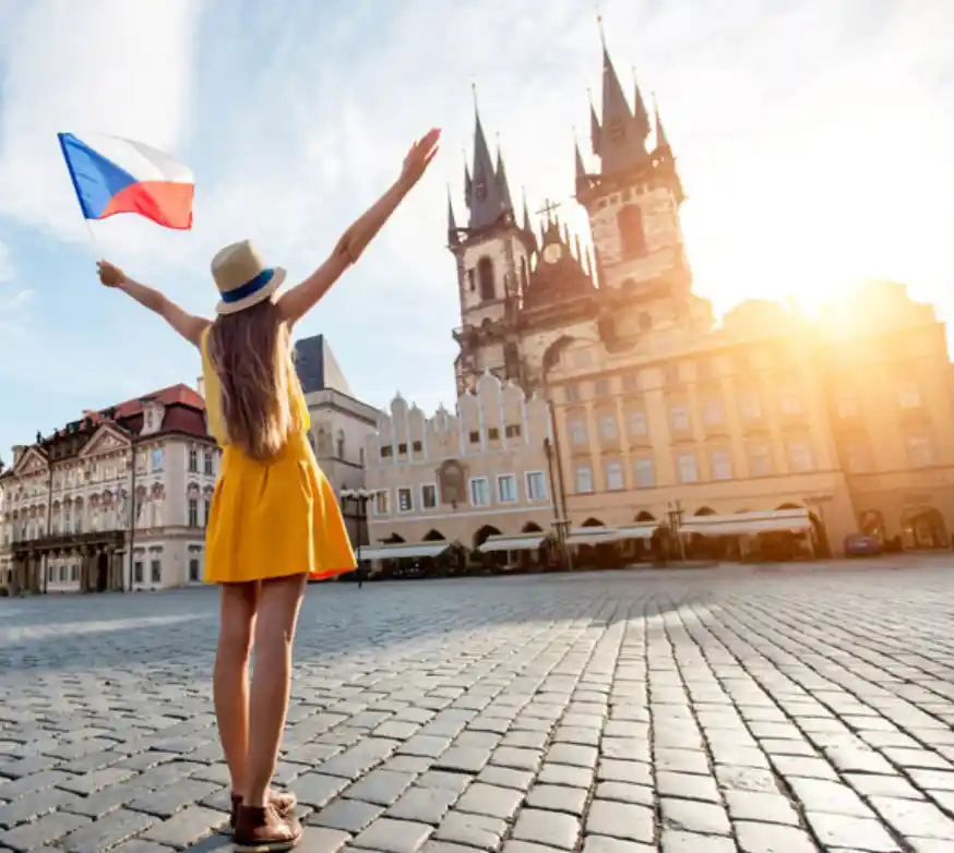 woman standing on prague old town square with arms in the air and a czech flag